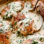 A golden brown chicken breast covered in a creamy lemon and cilantro sauce in a black skillet.
