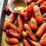 A tray of golden brown roasted carrots with garlic butter and fresh parsley