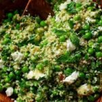 A bright green pearl couscous salad with peas, feta, and fresh basil dressing in a white bowl.
