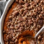 A golden brown sweet potato souffle in a white baking dish with a crunchy pecan crumble topping.