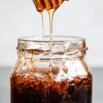 Golden homemade hot honey being drizzled from a wooden spoon into a glass jar.