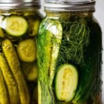 Two glass jars filled with sliced cucumbers in a clear brine with fresh dill and garlic.