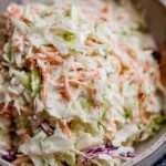 A bowl of creamy green cabbage and carrot coleslaw on a wooden table