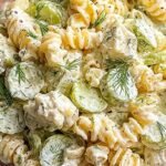 A bowl of creamy rotini pasta salad with diced dill pickles and cheddar cheese cubes