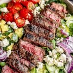 A vibrant Steak Cobb Salad arranged in rows with sliced steak, eggs, avocado, bacon, and blue cheese on a bed of romaine lettuce.