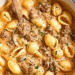 A skillet filled with creamy beef and shells pasta topped with melted cheddar cheese and fresh herbs