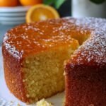 A golden Sicilian whole orange cake dusted with powdered sugar on a white plate