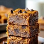 A batch of golden brown pumpkin bars sliced on a wooden board with autumn decorations