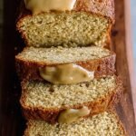 A golden brown loaf of cake mix banana bread sliced on a wooden board with mashed bananas nearby.