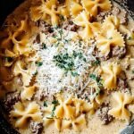 A skillet filled with bowtie pasta, browned ground beef, and a creamy garlic parmesan sauce topped with parsley.
