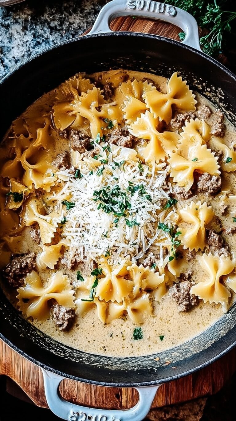 A skillet filled with bowtie pasta, browned ground beef, and a creamy garlic parmesan sauce topped with parsley.