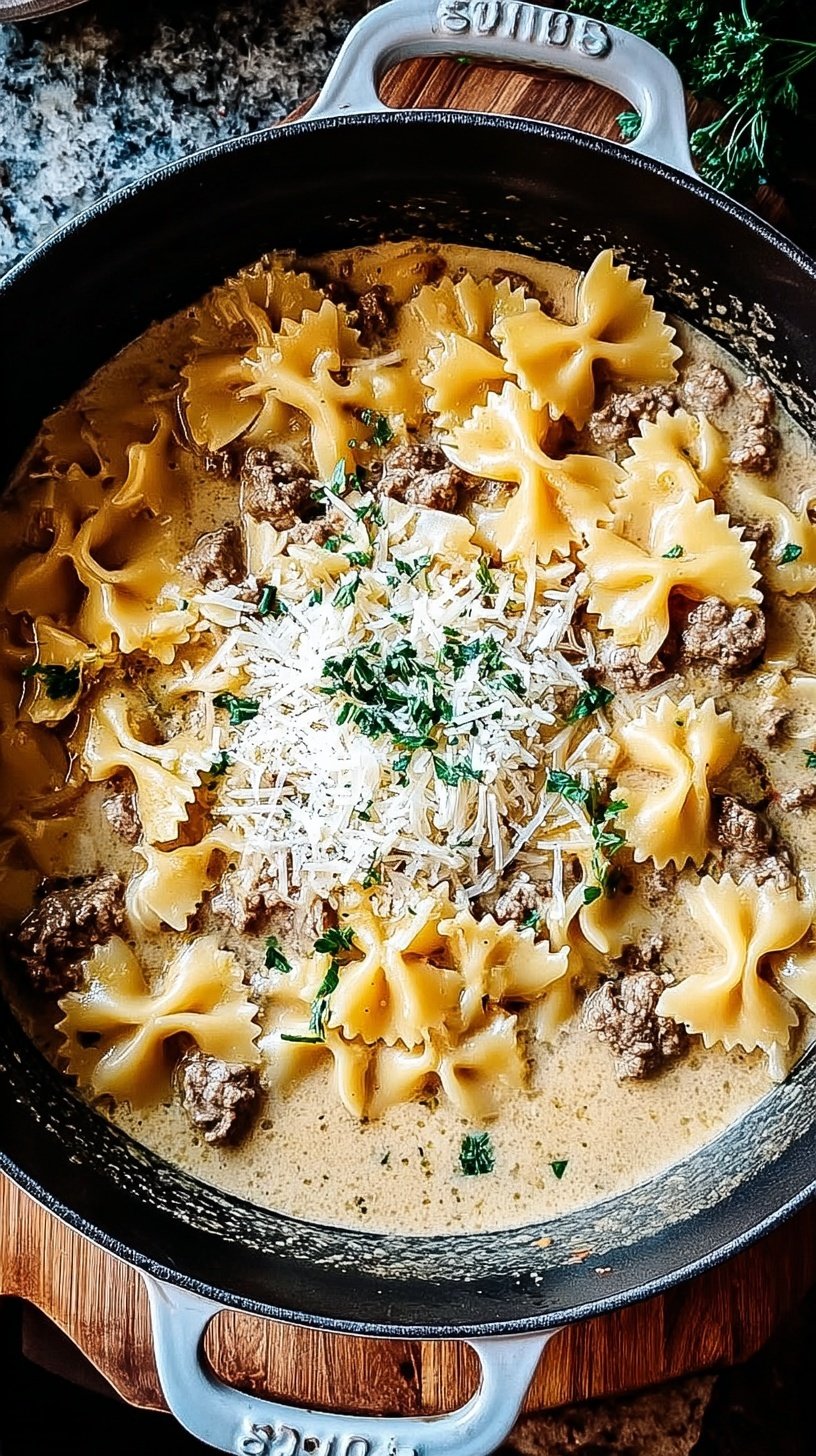 A skillet filled with bowtie pasta, browned ground beef, and a creamy garlic parmesan sauce topped with parsley.
