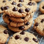 A stack of golden brown keto chocolate chip cookies with melty sugar-free chocolate chips on a parchment-lined baking sheet.