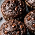 A tray of high-domed double chocolate chip muffins with melty chocolate chips on top.