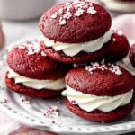 Two red velvet whoopie pies with white cream cheese frosting on a white plate