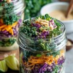 Four glass mason jars filled with layered colorful vegetables, chickpeas, and kale