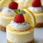 Twelve mini lemon cheesecakes in white liners topped with fresh lemon zest and cooling on a wire rack.