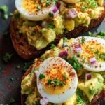 Two slices of whole grain toast topped with creamy avocado egg salad and a dusting of red paprika.