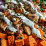 A vibrant bowl with roasted chicken, sweet potatoes, kale, and quinoa drizzled with tahini sauce.