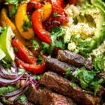 A colorful steak fajita bowl with seared steak, bell peppers, and cauliflower rice garnished with cilantro and lime.