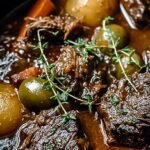A pot of rich Belgian beef stew with tender meat and dark gravy served with bread.