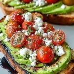 A slice of sourdough bread topped with mashed avocado, halved cherry tomatoes, and crumbled feta cheese.