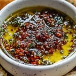 A shallow dish filled with herb-infused olive oil and balsamic vinegar for dipping bread.