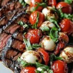 Juicy sliced balsamic grilled flank steak topped with fresh mozzarella, heirloom tomatoes, and basil on a platter.