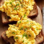 Fluffy scrambled eggs with visible cottage cheese curds and fresh chives in a pan.
