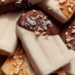 Creamy frozen healthy banana popsicles on a wooden board with fresh banana slices