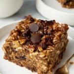 A square baking dish filled with golden brown baked oatmeal topped with blueberries and walnuts.