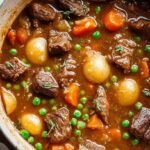 A steaming bowl of healthy beef stew with tender carrots, potatoes, and peas in a rich broth.