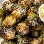 Golden brown crispy smashed Brussels sprouts on a baking sheet with melted parmesan cheese.