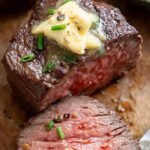 Two thick filet mignon steaks topped with melting butter and fresh rosemary in an air fryer basket.