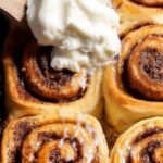 A tray of warm banana cinnamon rolls with creamy white icing and a cinnamon swirl