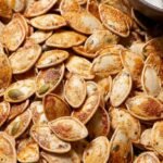 A bowl of golden brown roasted pumpkin seeds seasoned with garlic and paprika.