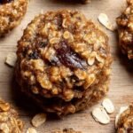 A tray of golden brown banana oat breakfast cookies with chocolate chips and walnuts on parchment paper.