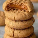 A stack of golden brown peanut butter cookies with fork crisscross patterns on a white plate.