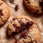 A stack of soft oat flour chocolate chip cookies with melty chocolate chips on a wire rack.