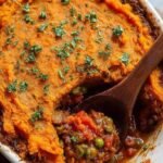 A bubbling dish of healthy shepherd's pie with a golden sweet potato topping and textured fork ridges.