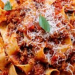 A bowl of wide pasta ribbons topped with rich, creamy chicken bolognese sauce and fresh basil.