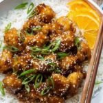Crispy orange chicken pieces in a glossy sauce with green onions and sesame seeds