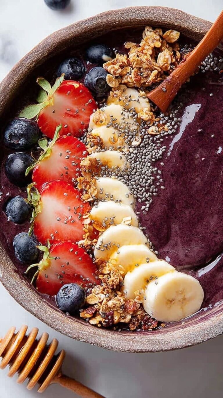 A thick and creamy purple acai bowl topped with granola, almond butter, and chia seeds in a white ceramic bowl.