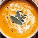 A bowl of creamy orange pumpkin sweet potato soup topped with a swirl of coconut milk and fresh herbs.