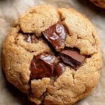 Freshly baked healthy chocolate chip cookies on a baking sheet with dark chocolate chips melting.