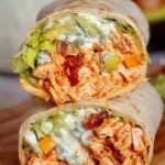 A sliced healthy buffalo chicken wrap with fresh romaine lettuce and creamy dressing on a white plate