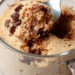 A warm chocolate protein mug cake in a white ceramic mug topped with fresh raspberries and a dollop of yogurt.