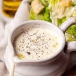 A bowl of creamy Greek yogurt Caesar dressing with a whisk and fresh lemon