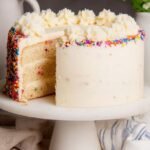 A double-layer healthy vanilla birthday cake topped with white whipped coconut cream frosting on a wooden cake stand.