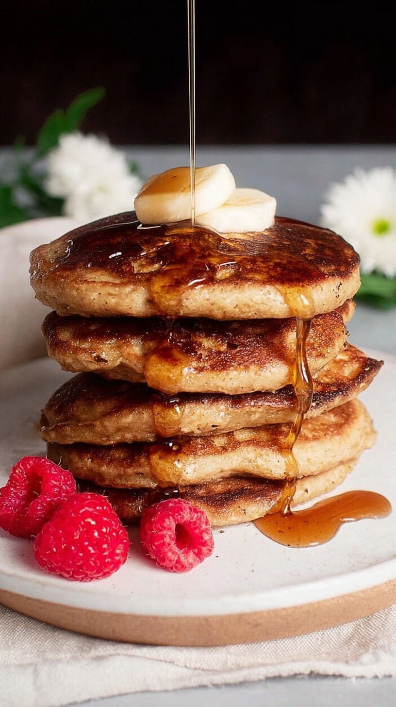 A stack of golden brown almond flour banana pancakes topped with fresh fruit and syrup.